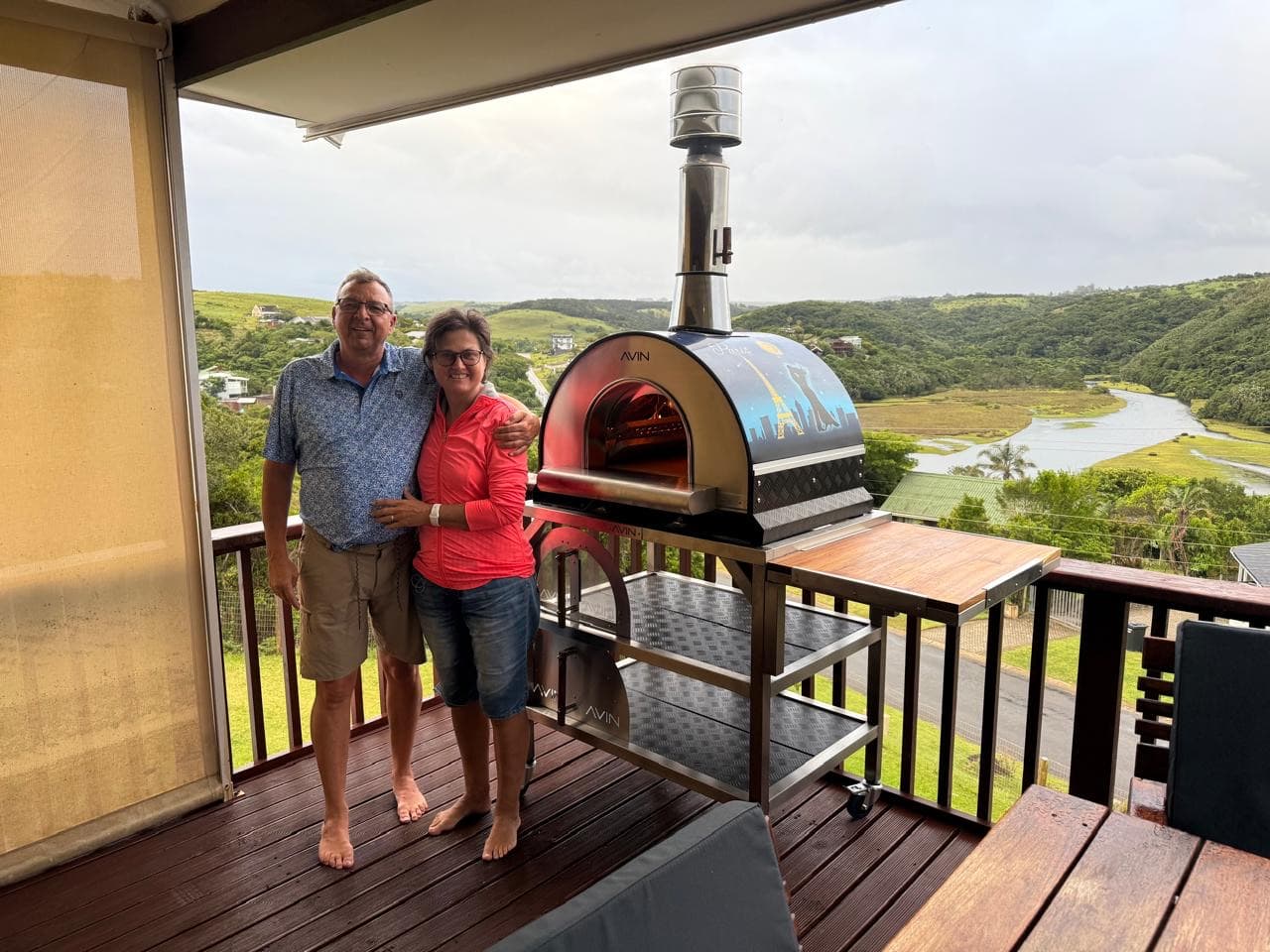 Two AVIN owners on their deck beside their AVIN, with the valley behind them